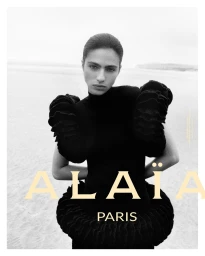 Model in black textured sculptural top standing on a sandy coast for Alaïa fall 2025 ad campaign.
