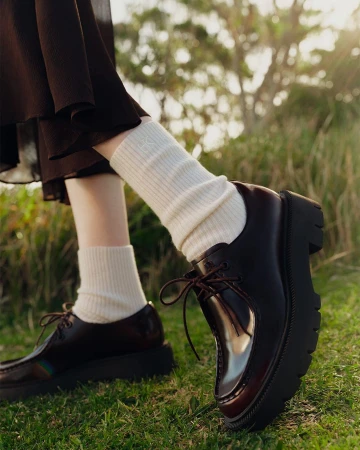 Close-up of brown leather platform shoes with white ribbed socks on grass outdoors