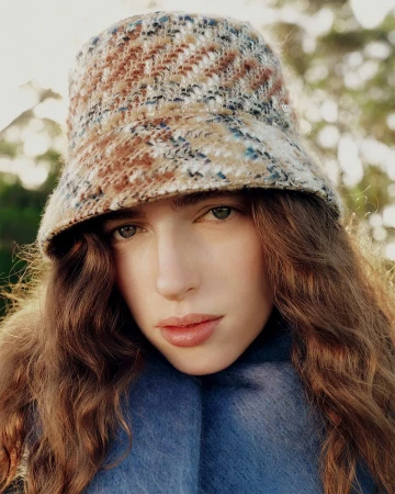 Close-up portrait of a woman wearing a textured tweed bucket hat and blue scarf outdoors in natural sunlight