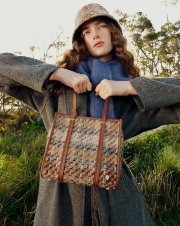 Woman wearing a tweed bucket hat and patterned coat holding a structured tweed handbag outdoors
