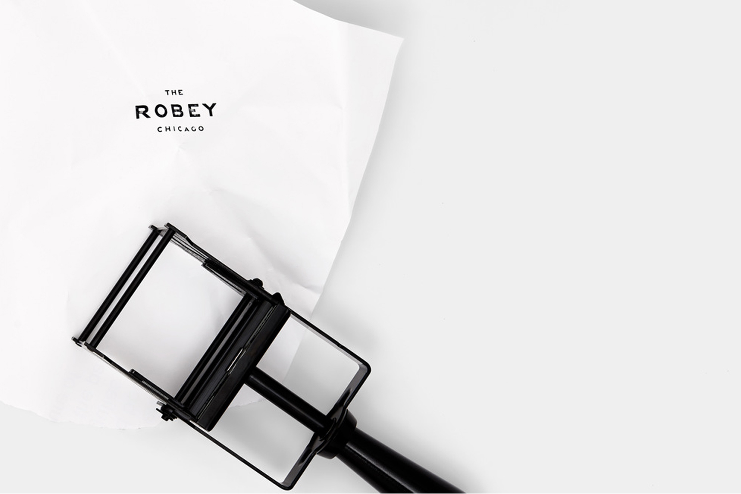 Black metal branding stamp beside crumpled white paper printed with The Robey Chicago logo on a clean white surface