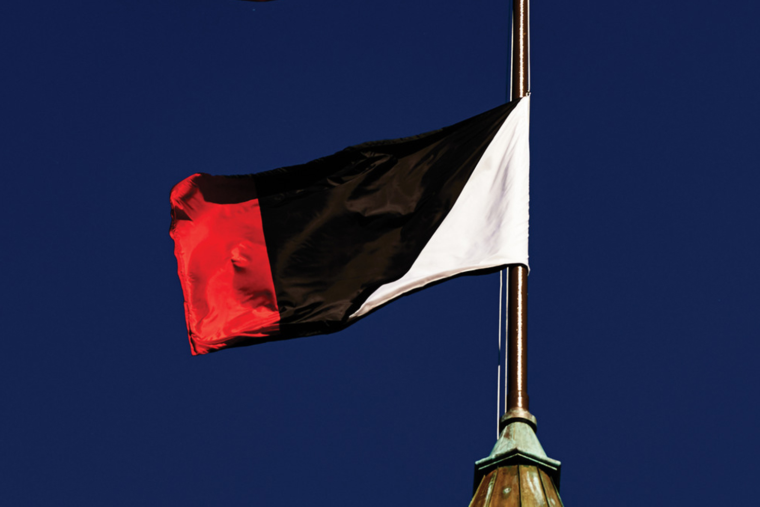 Flag with red, black, and white vertical sections flying on a pole against a deep blue sky.