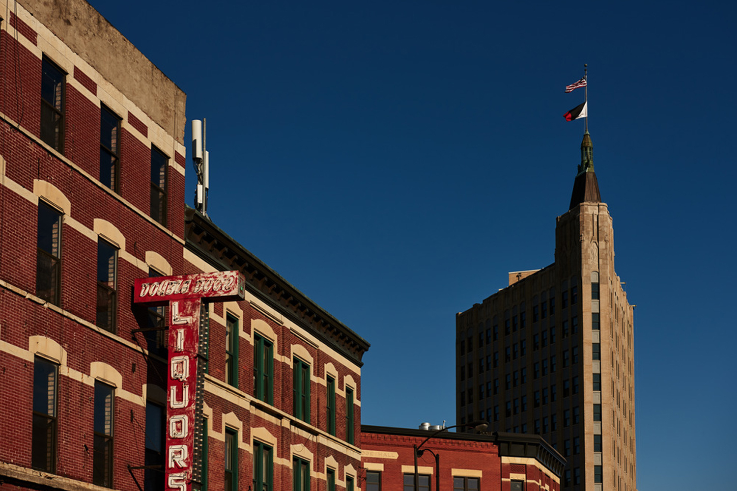 Red brick building exterior with vintage neon sign and tall art deco tower against a clear blue sky.