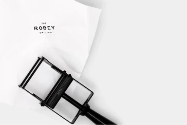 Black metal branding stamp beside crumpled white paper printed with The Robey Chicago logo on a clean white surface