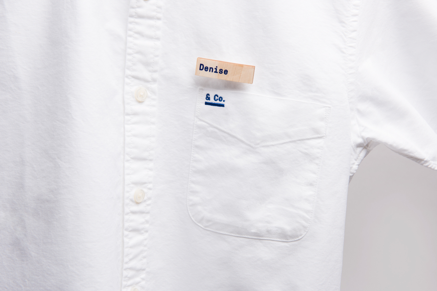 Close-up of a white button-down shirt with a name tag reading Denise and a pocket embroidered with Co.