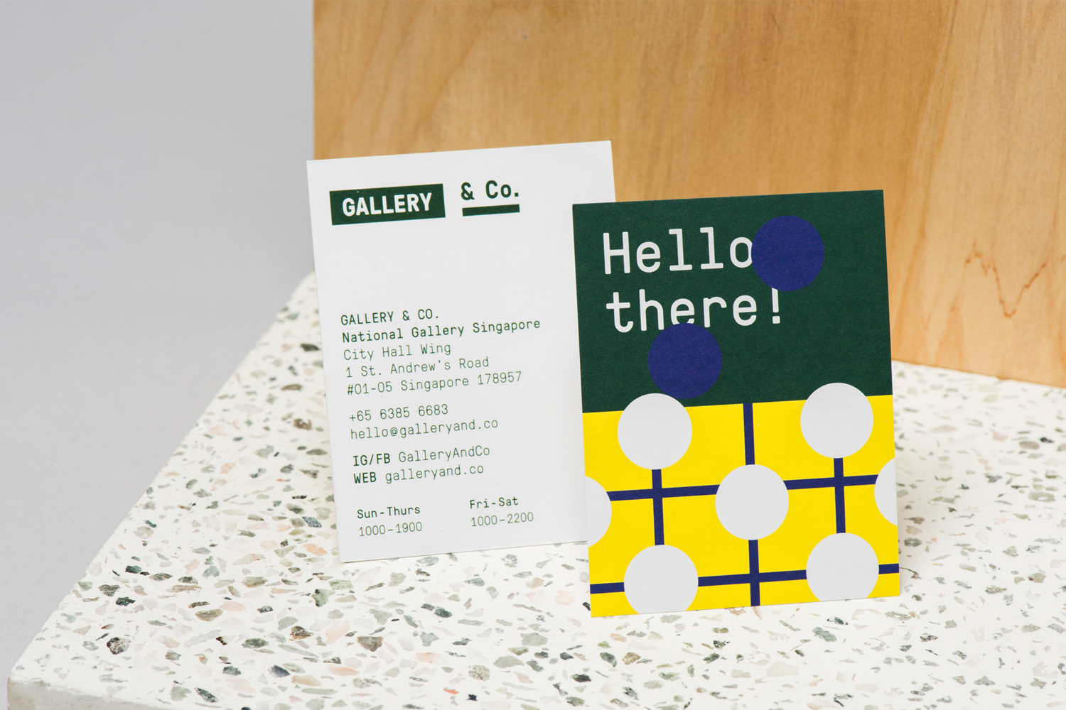 Two printed cards displaying the Gallery and Co brand identity resting on a textured speckled surface against a wooden backdrop.
