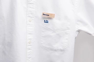 Close-up of a white button-down shirt with a name tag reading Denise and a pocket embroidered with Co.