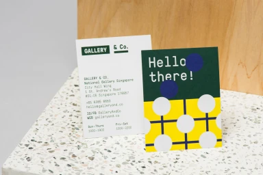 Two printed cards displaying the Gallery and Co brand identity resting on a textured speckled surface against a wooden backdrop.