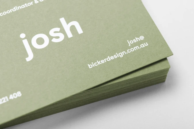 Close-up of a stacked stack of olive green business cards with white sans-serif typography showing the name josh
