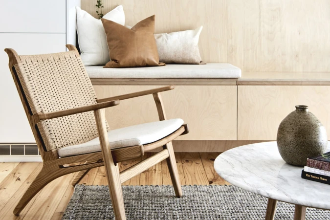 Wooden armchair with woven cane seat next to a marble coffee table in a light wood interior setting.
