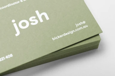 Close-up of a stacked stack of olive green business cards with white sans-serif typography showing the name josh