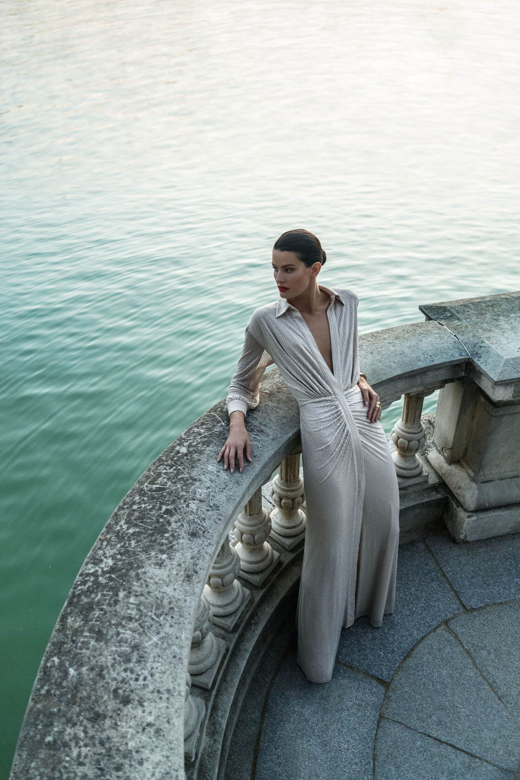 Model Isabeli Fontana leaning on a stone balustrade above water for BCBGMAXAZRIA Fall 2025 campaign, photographed by Juankr.