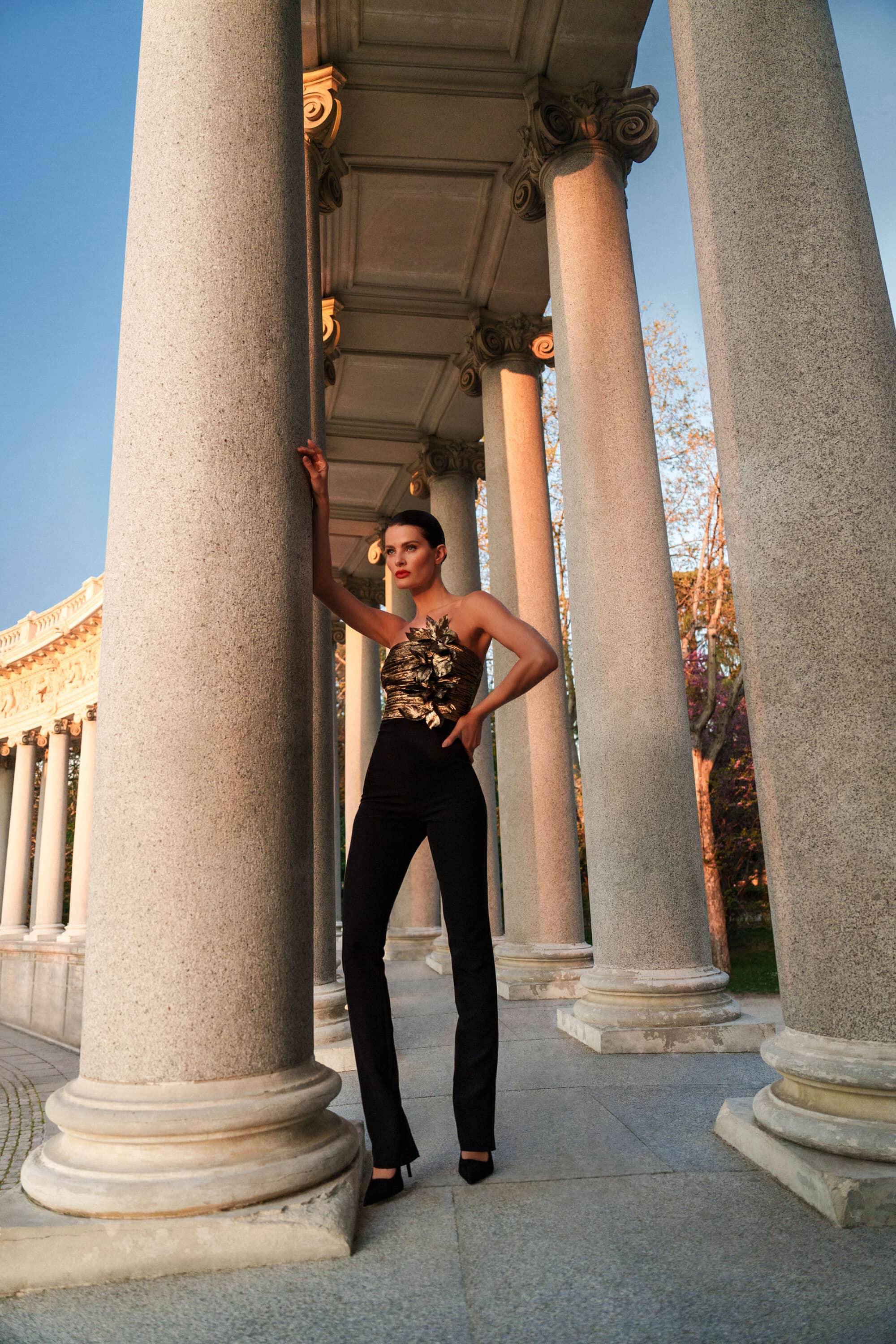 Isabeli Fontana in a black jumpsuit leaning against neoclassical columns for BCBGMAXAZRIA