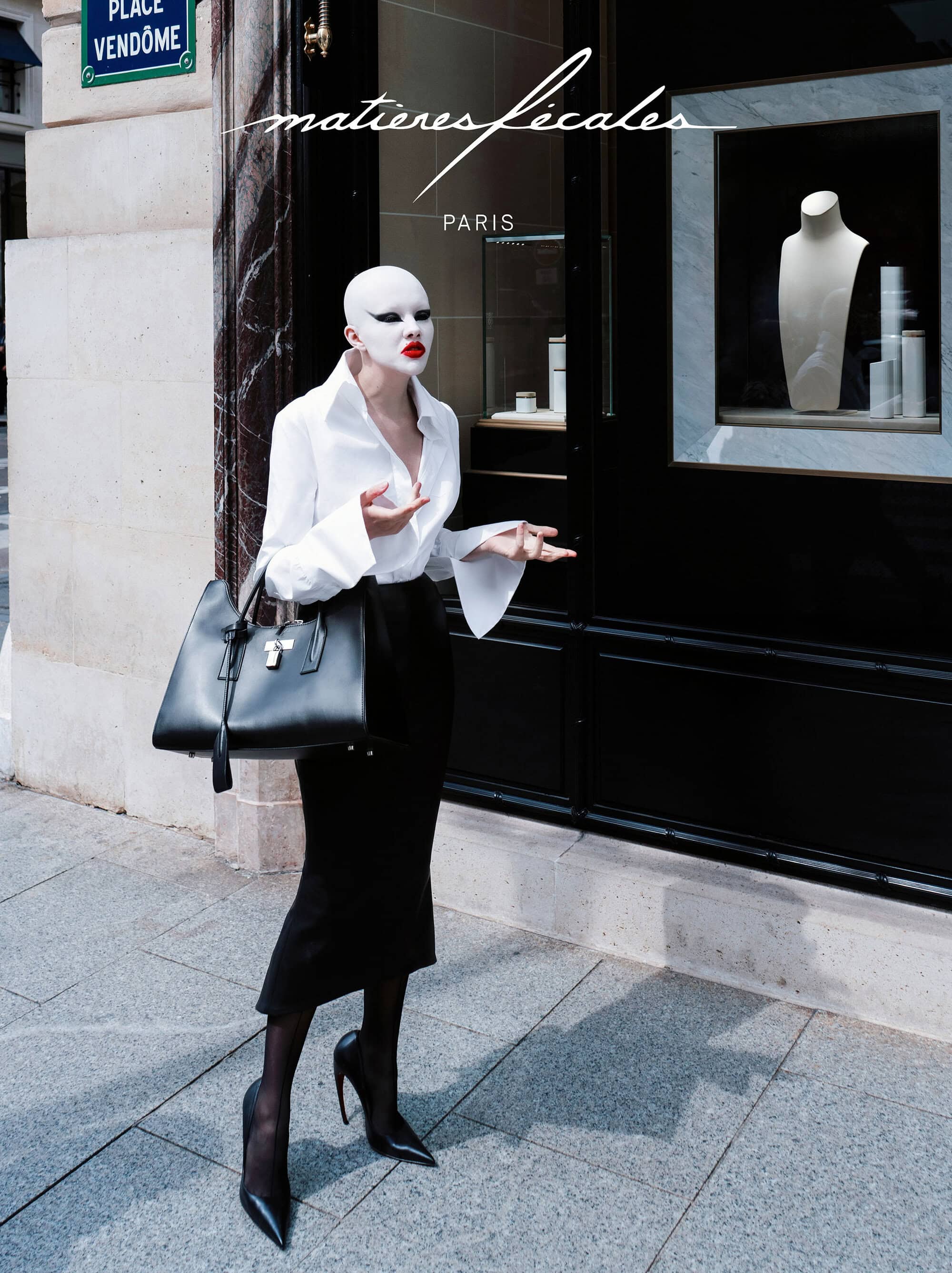 Model with white face makeup wearing a white button-down shirt and black skirt outside a storefront in Paris