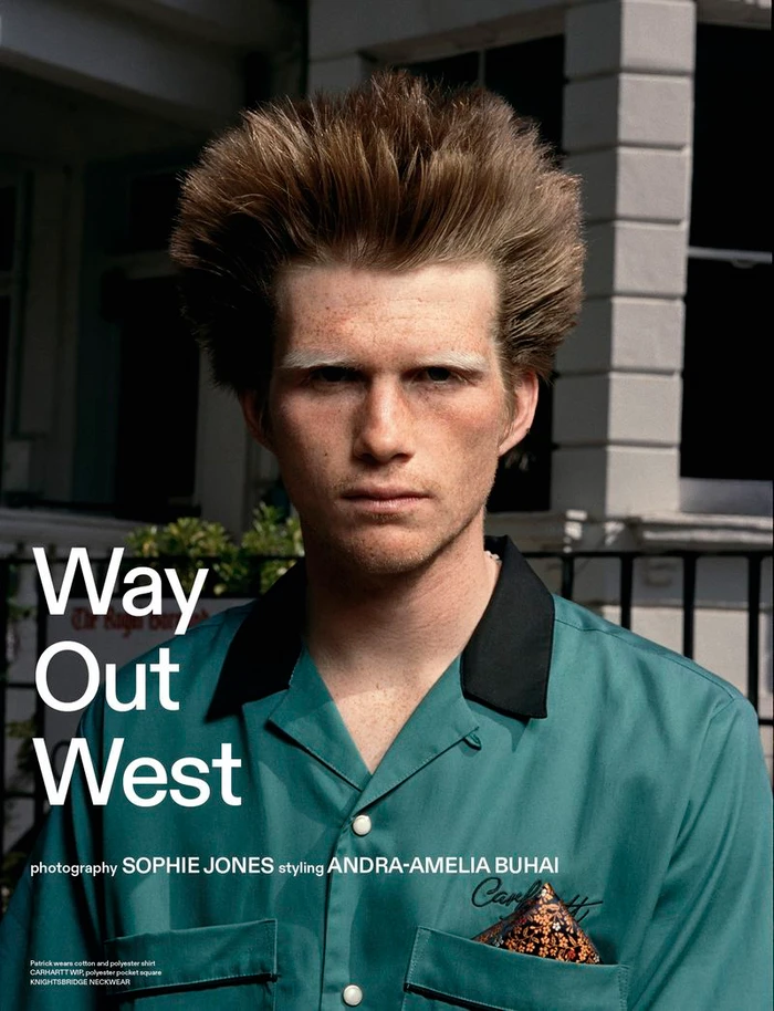 Close-up portrait of a man with voluminous brown hair and bleached eyebrows wearing a green collared shirt