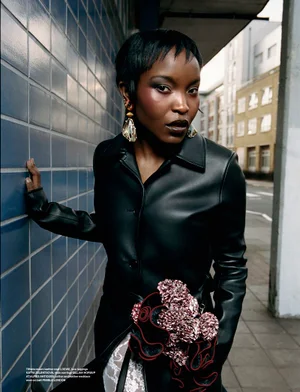 Black woman wearing black leather jacket posing against blue tiled wall for Dazed Magazine editorial