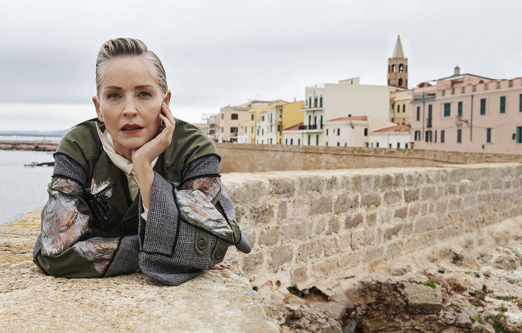 Sharon Stone leaning on a stone wall overlooking a coastal town in an ad campaign for Antonio Marras