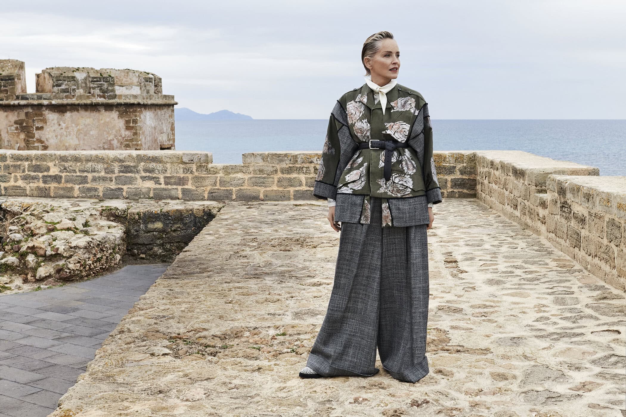 Sharon Stone standing on a stone rampart overlooking the sea for Antonio Marras Fall 2025 ad campaign