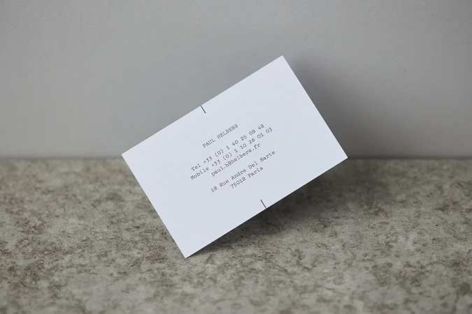 White business card with typewriter text resting at an angle on a textured stone and plain wall background.
