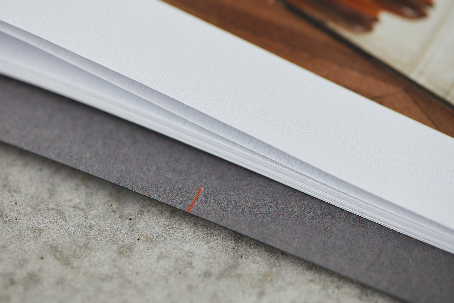 Macro shot of stacked white paper sheets and a dark grey textured cover with a single orange alignment mark.