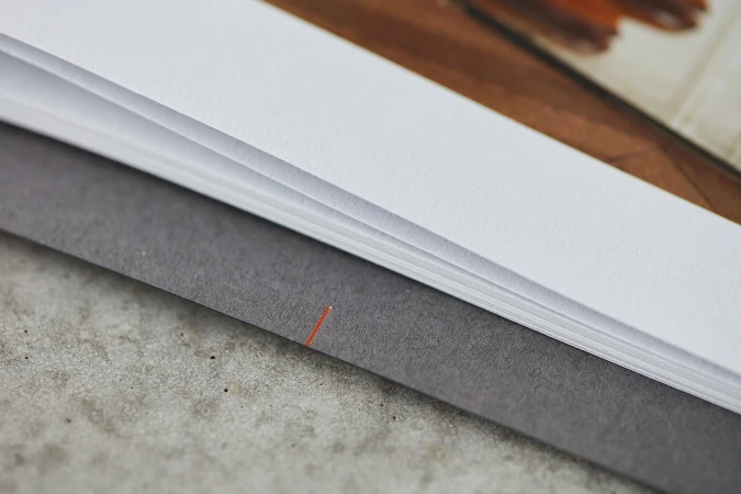 Macro shot of stacked white paper sheets and a dark grey textured cover with a single orange alignment mark.