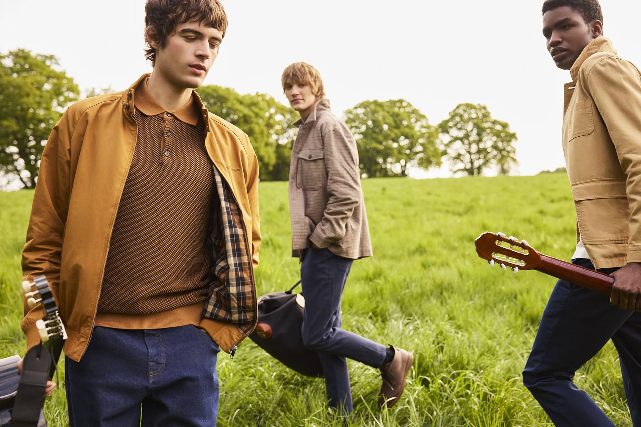 Three young men walking through a grassy meadow carrying guitars and bags for a Ben Sherman campaign