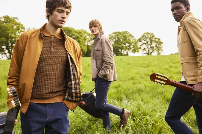 Three young men walking through a grassy meadow carrying guitars and bags for a Ben Sherman campaign