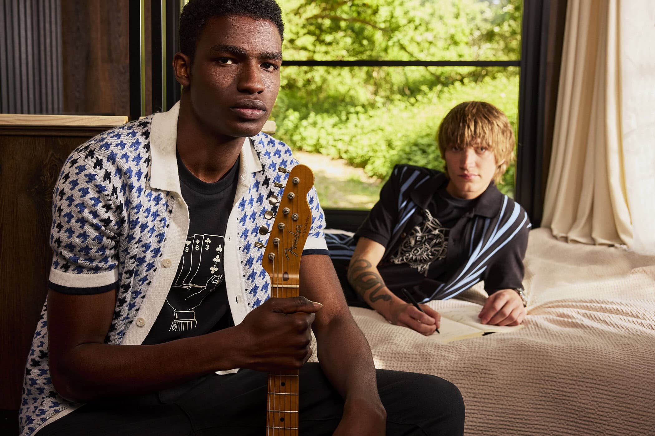 Two male models posing indoors, one holding a guitar near a window with a green foliage view for Ben Sherman.