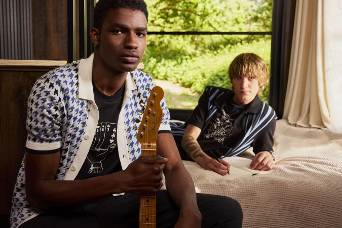 Two male models posing indoors, one holding a guitar near a window with a green foliage view for Ben Sherman.