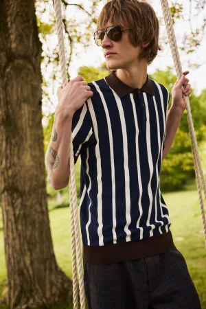 Young man in a striped polo shirt wearing sunglasses while holding rope on an outdoor swing in a park