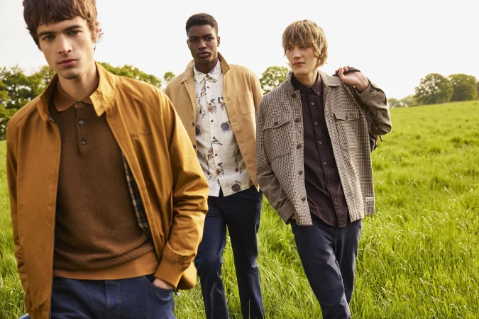 Three male models in casual outerwear walking together through a green meadow for the Ben Sherman Signature fall campaign
