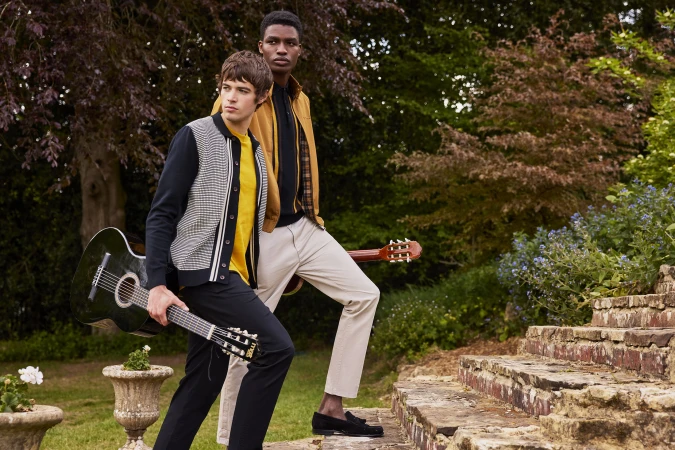 Two male models holding acoustic guitars posing outdoors on stone steps beside garden foliage for Ben Sherman.