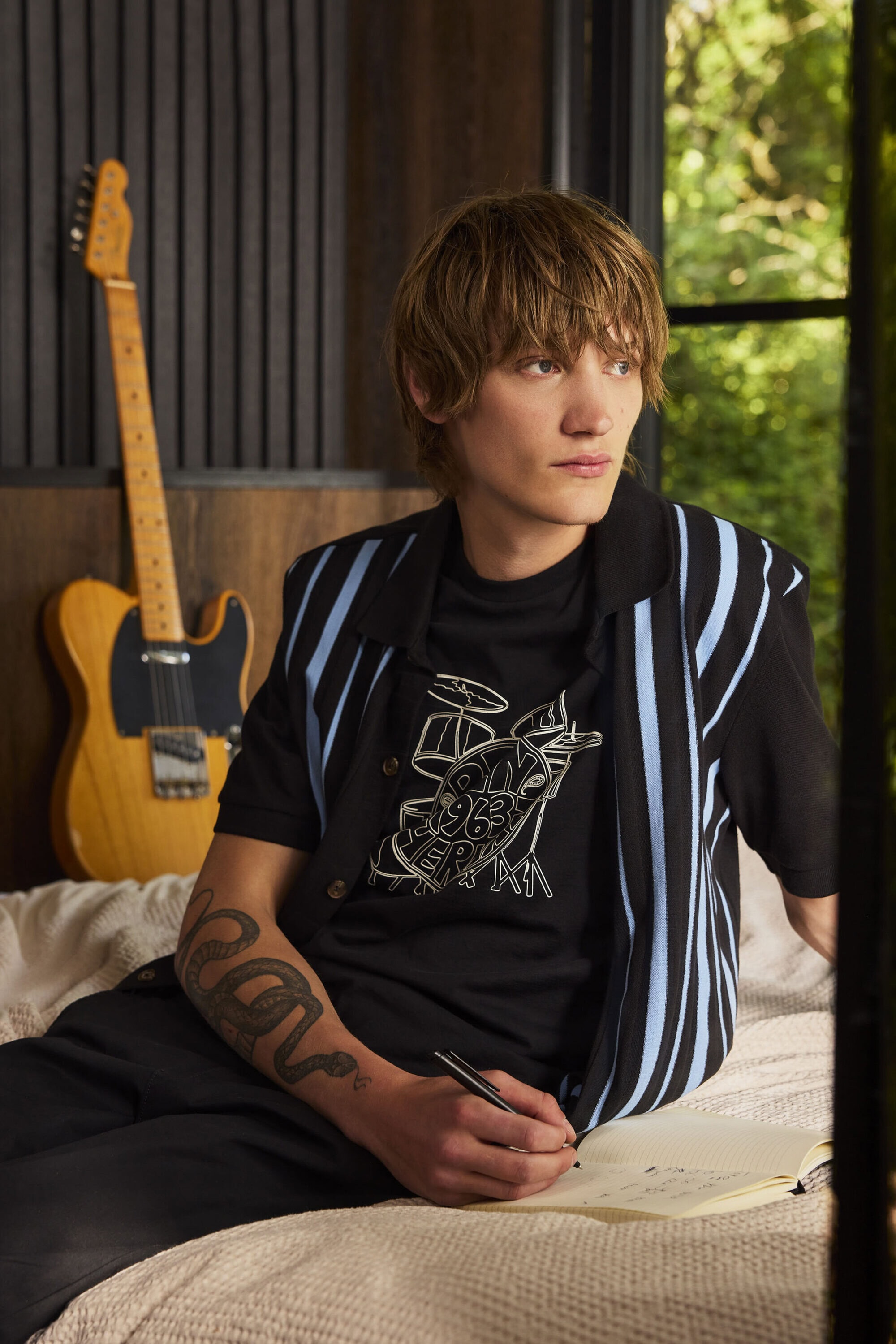 Young man writing in a notebook on a bed next to an electric guitar for Ben Sherman