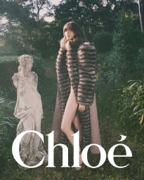 Model standing outdoors next to a classical stone statue wearing a long patterned coat for Chloe winter 2025 campaign