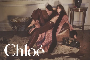 Model Grace Hartzel reclining in an armchair wearing a quilted coat and leather pants with a dark handbag for Chloé.