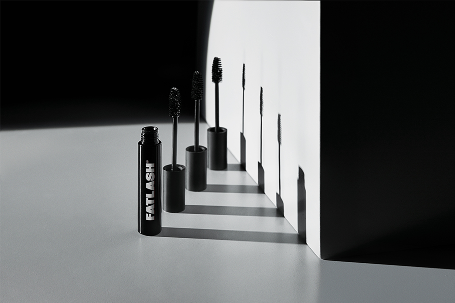 Mascara tubes with ascending wand heights arranged in perspective against a white corner wall casting long shadows