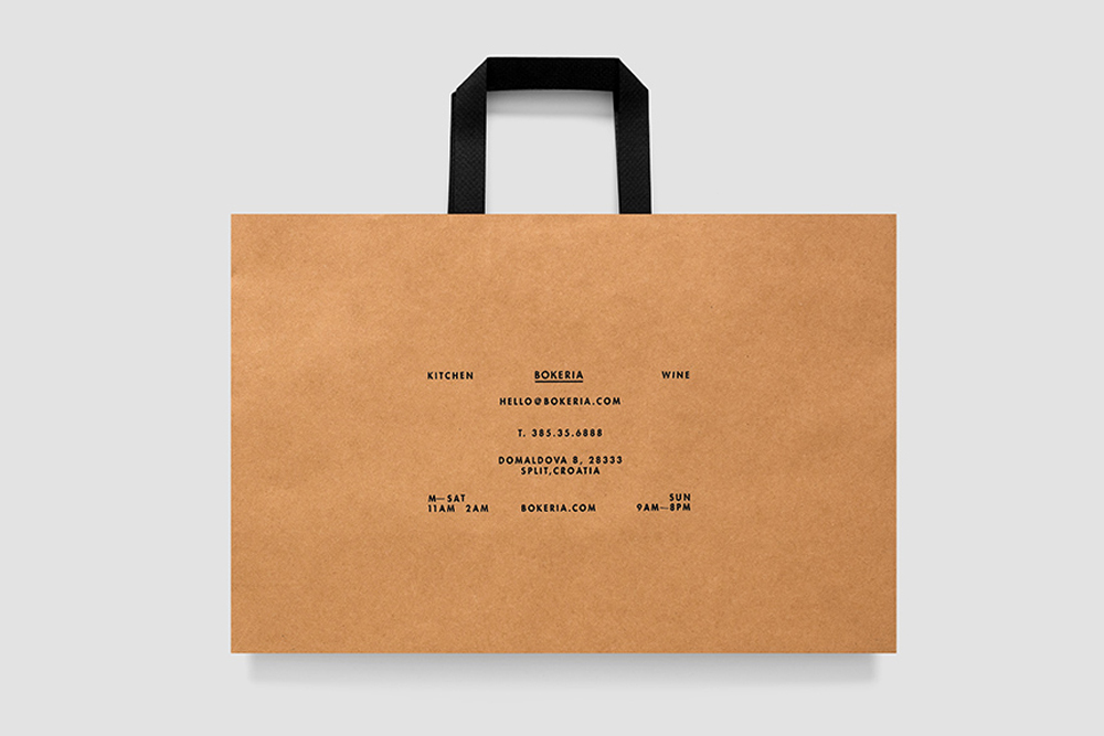 Kraft paper shopping bag with black fabric handles and centered typography against a solid white background