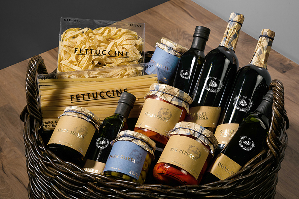 Wicker gift basket filled with Bokeria artisanal food products including wine bottles, pasta packages, and jars of olives.