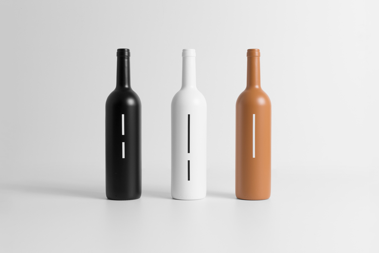 Three minimalist bottles in black, white, and terracotta standing upright against a plain light grey studio background.