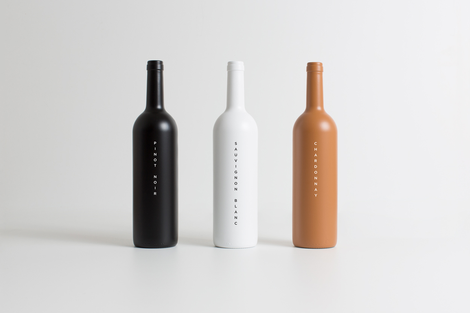 Three opaque wine bottles in black, white, and terracotta standing upright in a row against a plain light background.