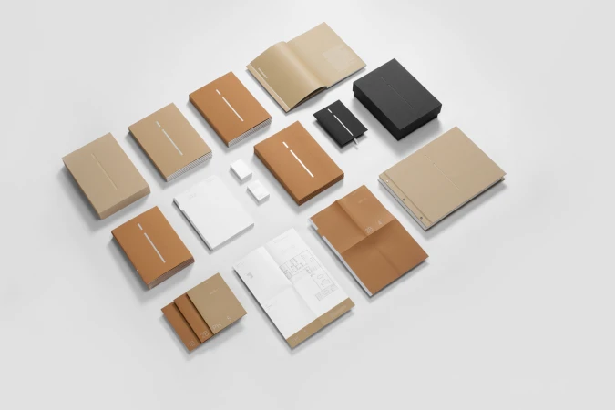 Flat lay of corporate stationery items including notebooks, folders, and cards in brown, tan, white, and black on a white background.