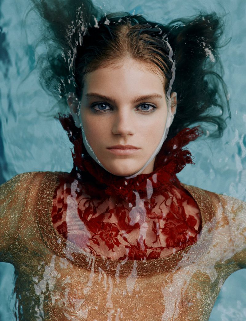 Portrait of a woman in water with dark hair, light skin, and a red lace collar, creating a surreal and captivating underwater fashion shot.
