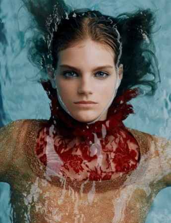 Portrait of a woman in water with dark hair, light skin, and a red lace collar, creating a surreal and captivating underwater fashion shot.