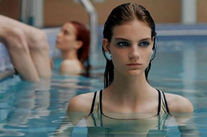 Wet-haired female model in a swimming pool wearing earrings with other models in the background for Dazed Magazine