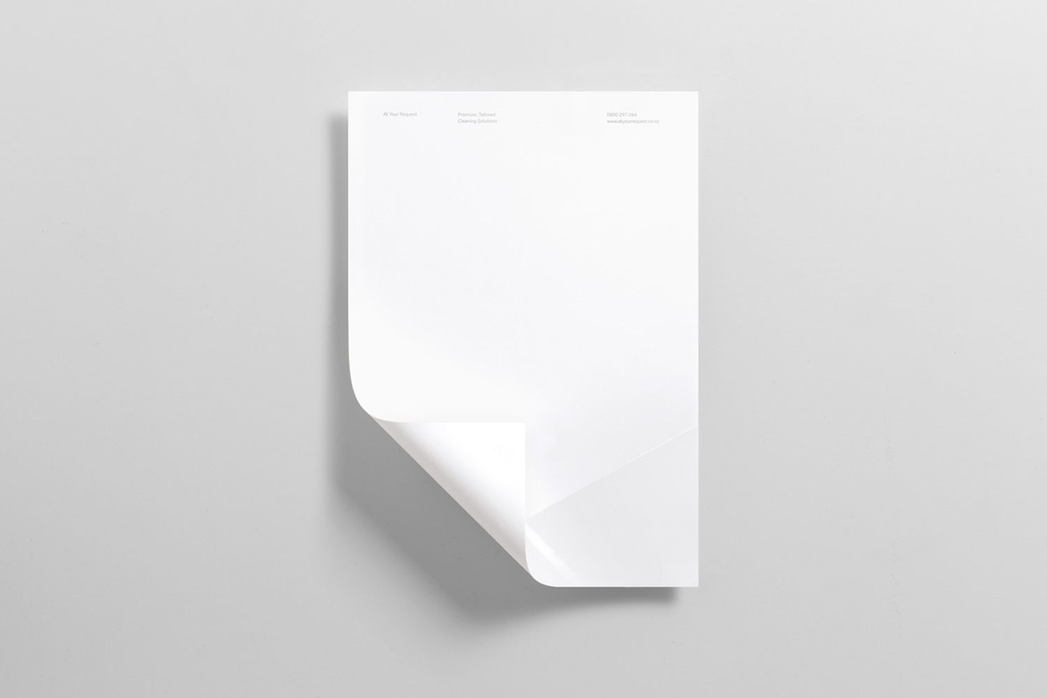 A blank white letterhead sheet with a curled bottom-left corner resting on a minimal light grey background.