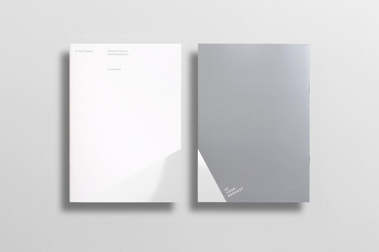 Two minimalist paper brochures with clean typography resting on a neutral grey background with soft drop shadows.