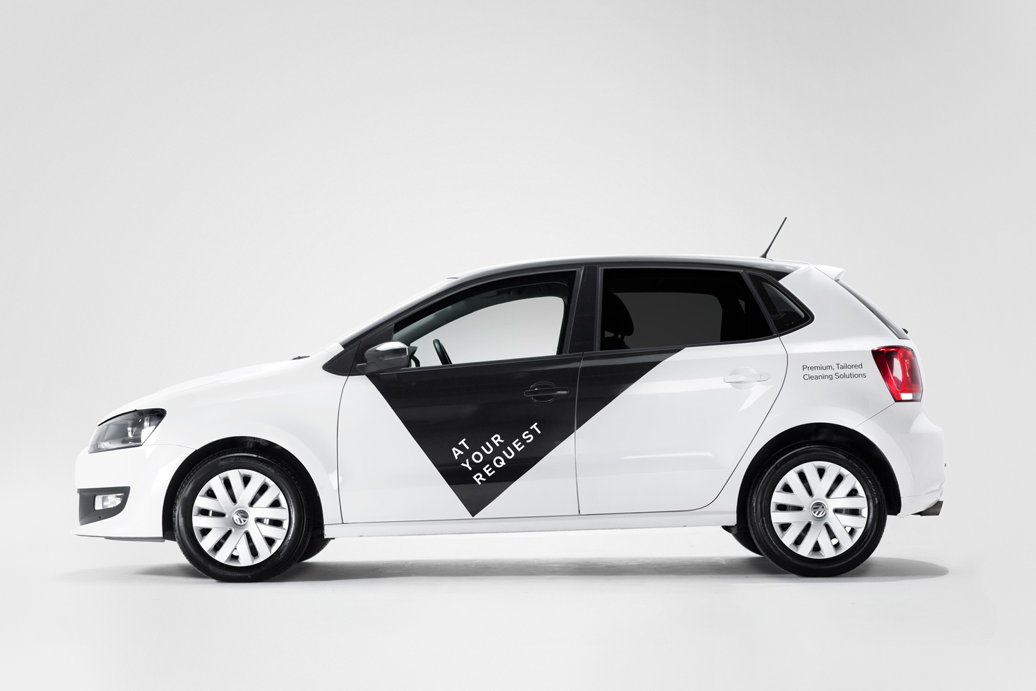 Profile view of a white hatchback car with black branded panel and At Your Request logo on a seamless white background.