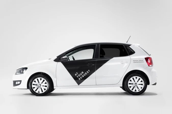 Profile view of a white hatchback car with black branded panel and At Your Request logo on a seamless white background.