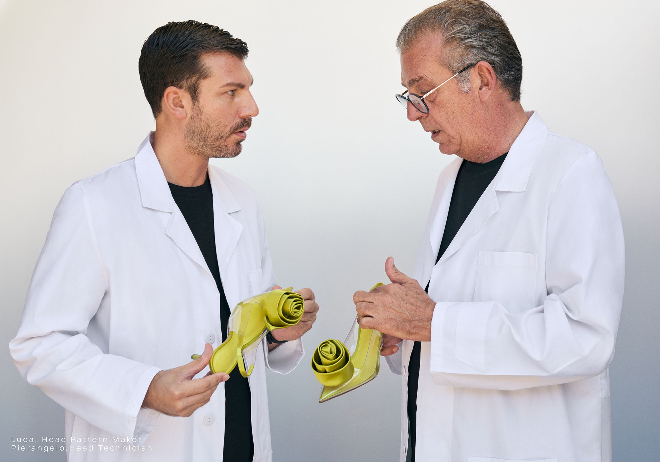 Two men in white lab coats holding lime green heeled shoes against a plain white background