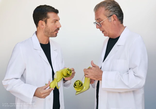 Two men in white lab coats holding lime green heeled shoes against a plain white background